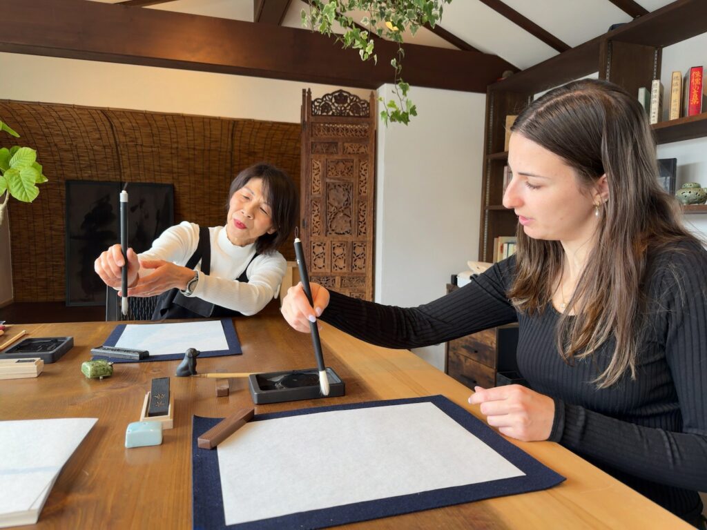 Guest from the United States learning how to hold a calligraphy brush from the instructor at Atelier & Gallery Ichirin in Kamakura