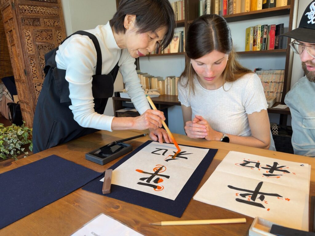 Instructor explaining kanji brush strokes to guests from Germany during a Japanese calligraphy lesson at Atelier & Gallery Ichirin