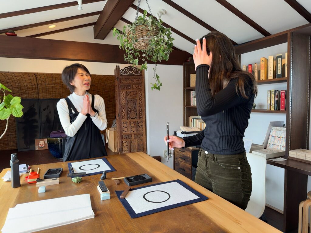Guest from the United States practicing brush strokes by drawing a circle during a Japanese calligraphy lesson in Kamakura