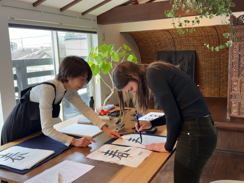 Guest from the United States practicing writing kanji characters with guidance from the instructor at Atelier & Gallery Ichirin in Kamakura