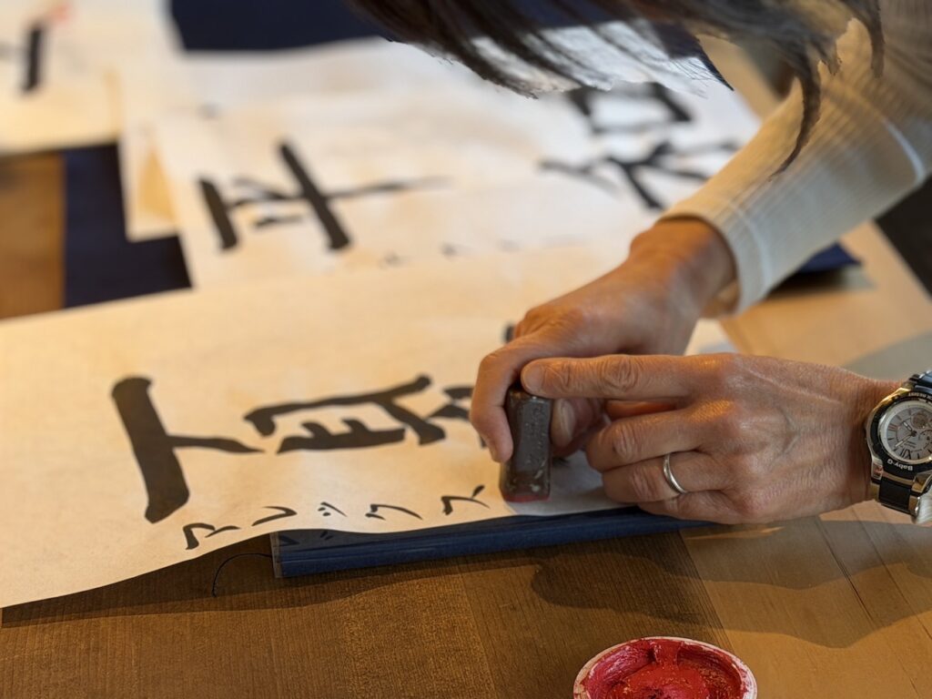 Instructor stamping a traditional seal on completed Japanese calligraphy artwork in Kamakura