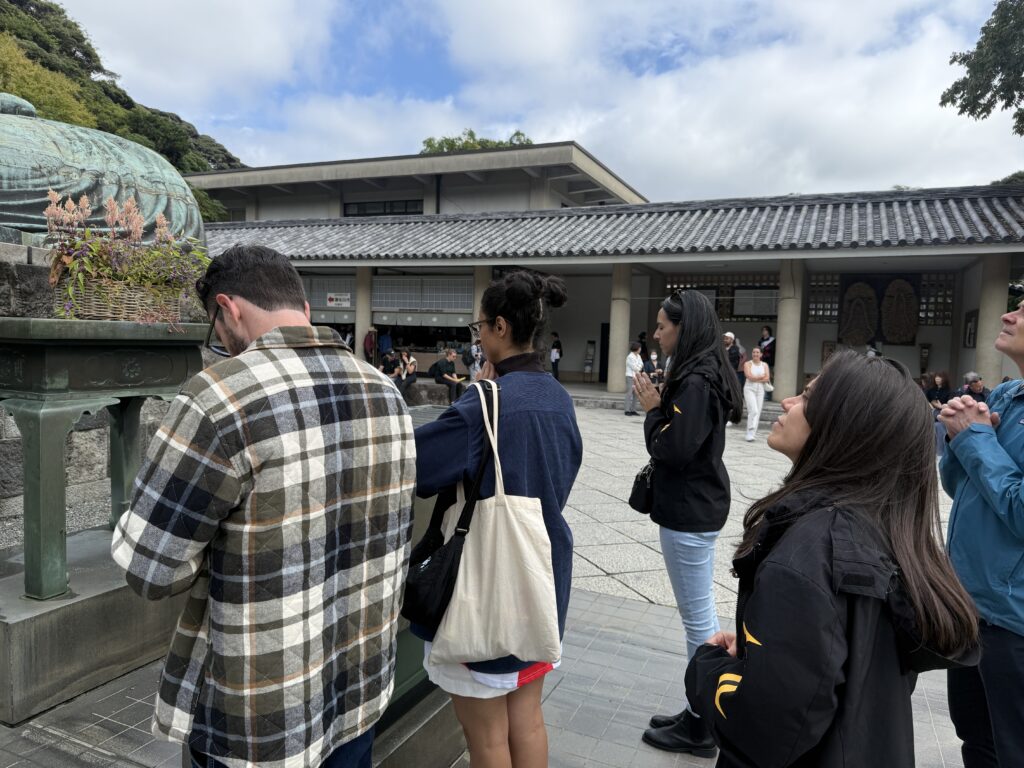 Guests praying with hands together in front of the Great Buddha of Kamakura.